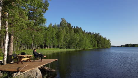 woman read book on sunny summer day near lake coast in scandinavia, aerial view