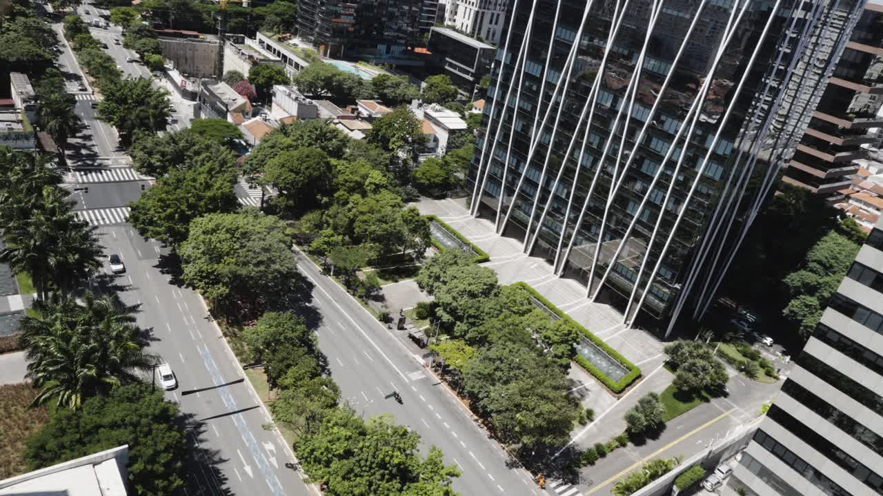 Dutch angle of low traffic on tree-lined streets in São Paulo, Brazil. The streets sit next to high-rise ornate glass and steel office buildings.