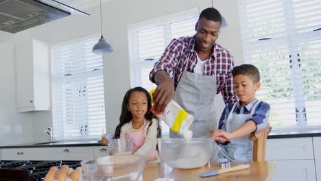 Vista-Frontal-Del-Padre-Negro-Con-Sus-Hijos-Preparando-Comida-En-La-Cocina-4k