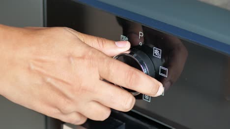 la mano de la mujer estableciendo el control de temperatura en el horno