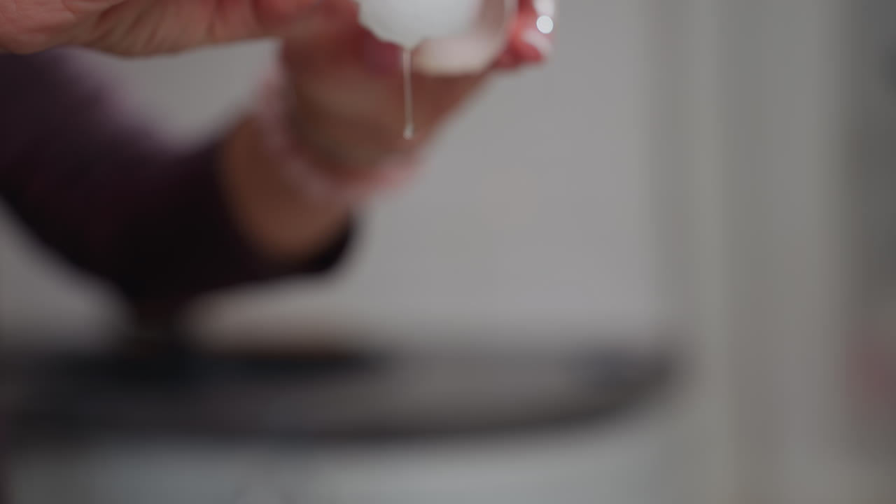 primer plano de las manos rompiendo un huevo, permitiendo que su contenido gotee hacia abajo en un recipiente, la yema de huevo fresca y la clara de huewo fluyen suavemente a medida que la cáscara se separa suavemente