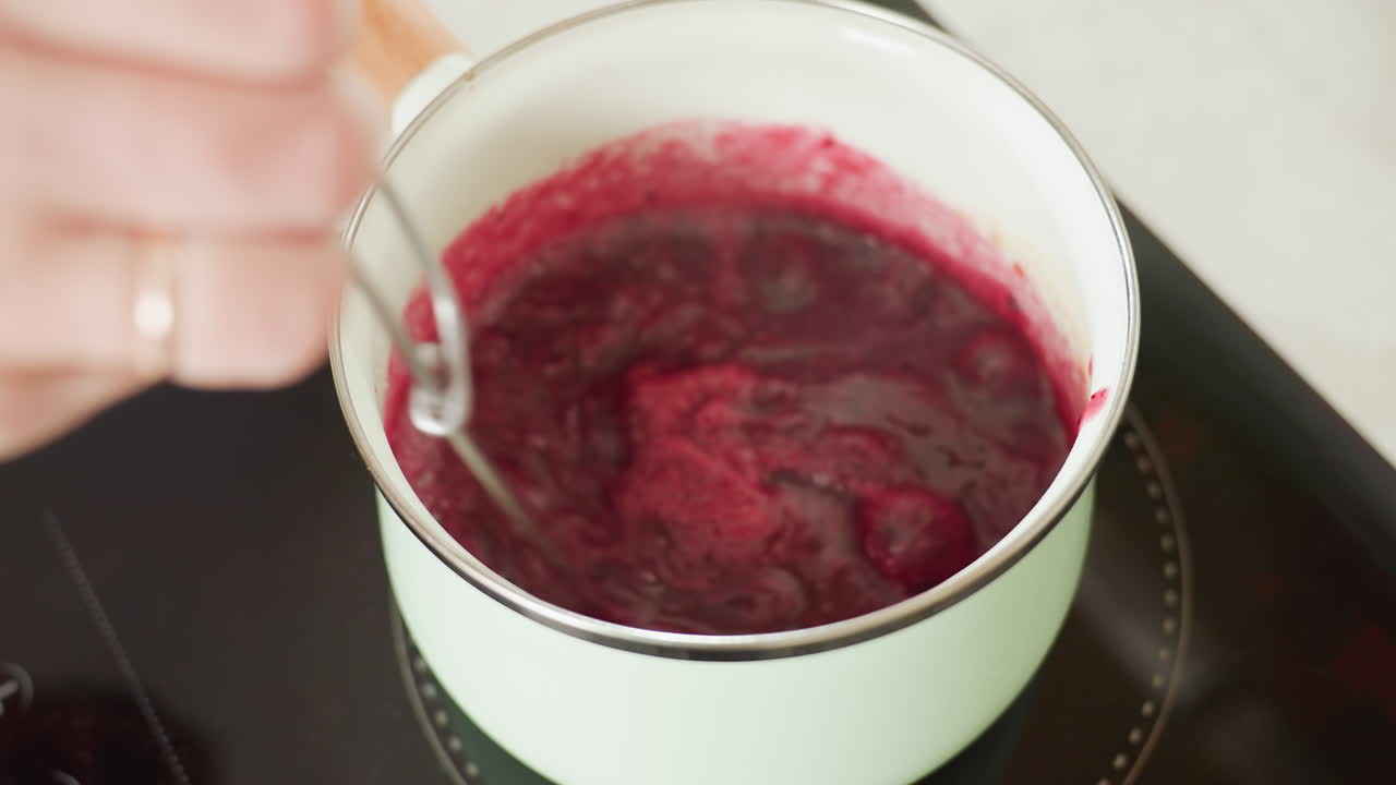 Close up of thick red soup or sauce bubbling in pastel green pot on electric stove with twister utensil partially submerged, capturing cooking texture, heat activity, and rich color in home kitchen