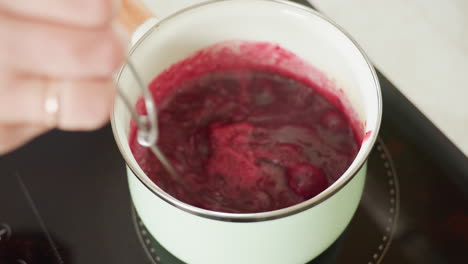 close up of thick red soup or sauce bubbling in pastel green pot on electric stove with twister utensil partially submerged, capturing cooking texture, heat activity, and rich color in home kitchen