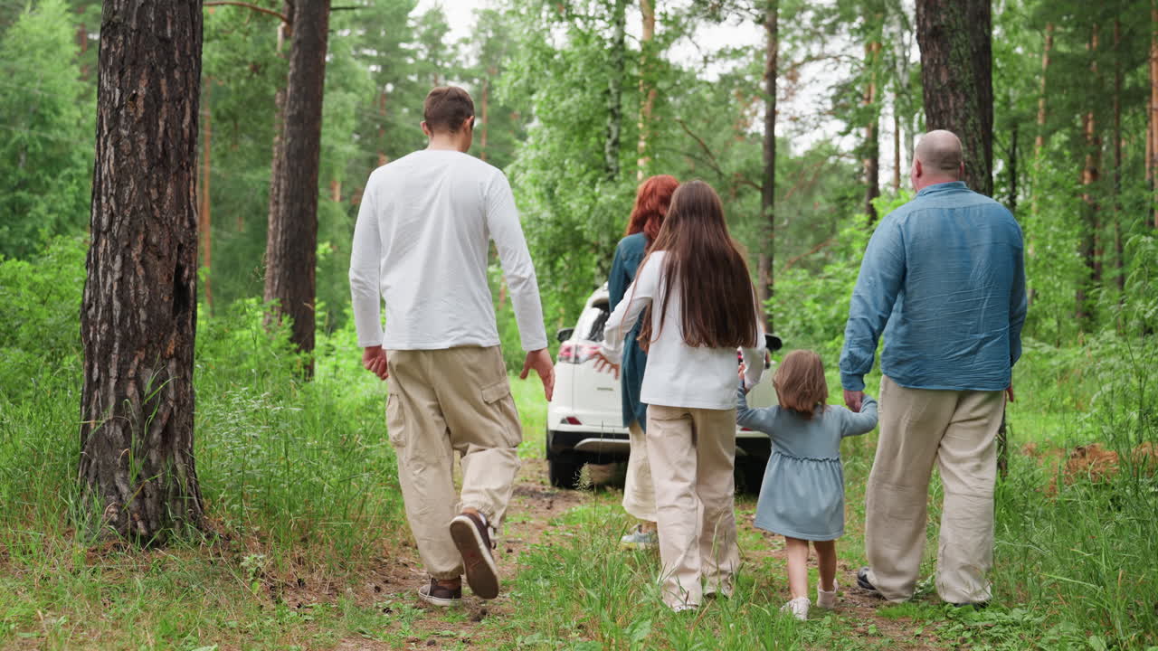 초록색 숲에서 주차된 차를 향해 손을 잡고 함께 걸으며 자연을 즐기는 가족의 뒷모습은 단합, 휴식, 연결과 행복으로 가득 찬 평화로운 야외 순간을 보여줘요