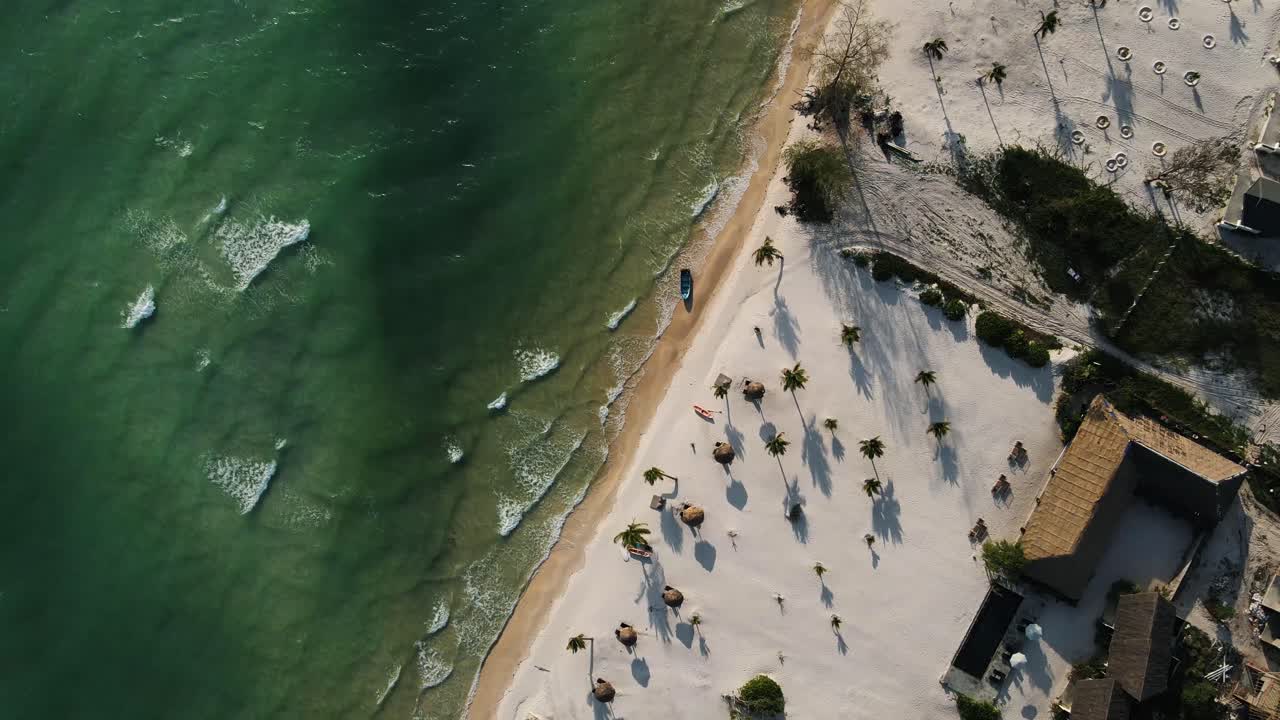 grandes olas del mar azul claro llegan a la hermosa playa de arena blanca donde un bote de remos de madera descansa en el oleaje en la isla de koh rong en camboya