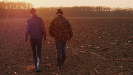 Middle-Aged-Farmer-With-His-Son-Walking-Across-The-Field-At-Sunset-Family-Farm-Concept