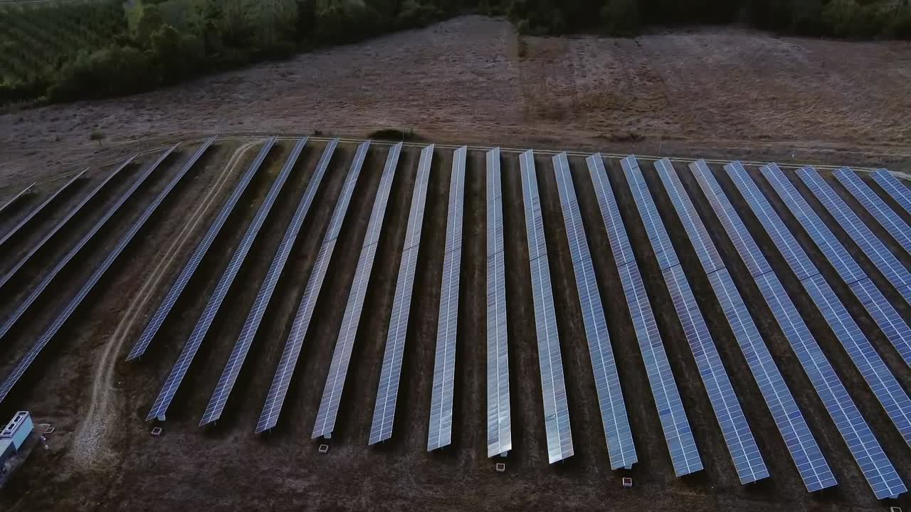 panorámica aérea sobre el conjunto de paneles solares de la granja con exuberantes campos verdes y colinas en el horizonte