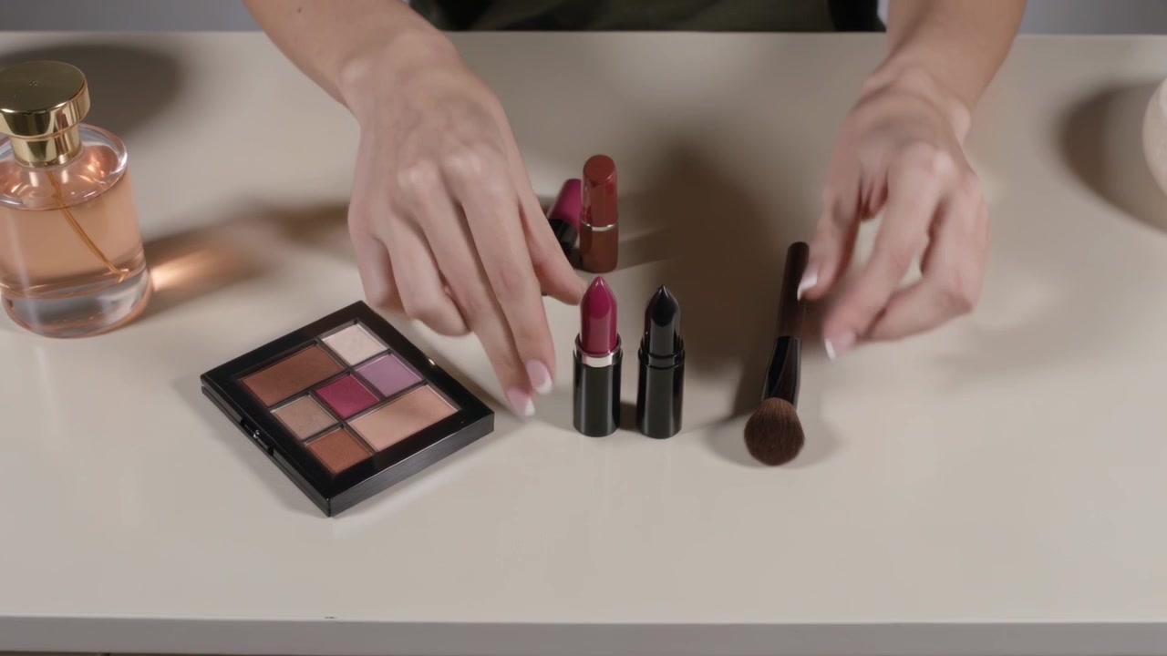 Entering frame, woman's hands in dark top lifting and arranging lipsticks, brush on vanity for demo
