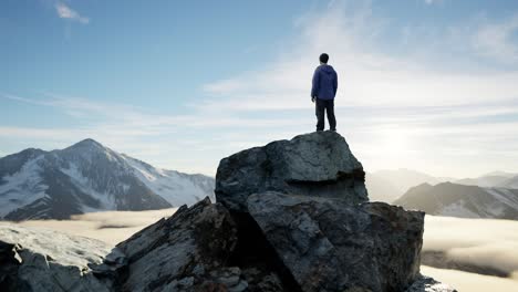 adventurous male hiker standing on dramatic rocky cliff, low clouds and snowy mountain landscape