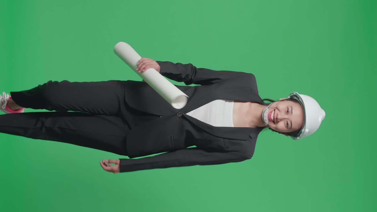 Smiling Asian Female Engineer With Safety Helmet And Blueprint Walking In The Green Screen Studio