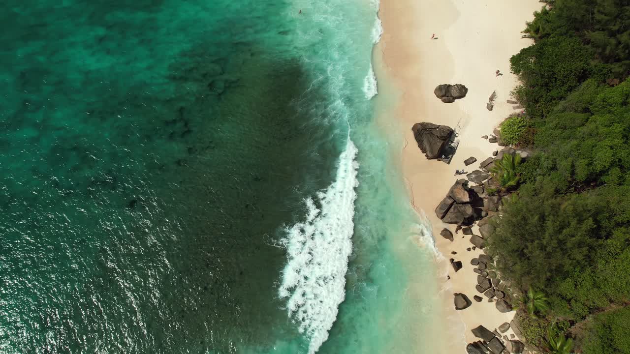 Ripresa con drone di Mahé, Seychelles, di clienti che camminano sulla spiaggia vicino a rocce di granito, giornata di sole, acqua turchese.