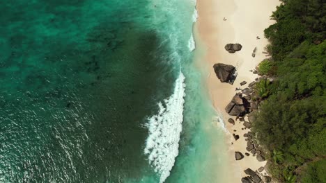 Mahe-Seychelles-drone-shot-of-clients-walking-on-the-beach-near-granite-rocks,-sunny-day,-turquoise-water