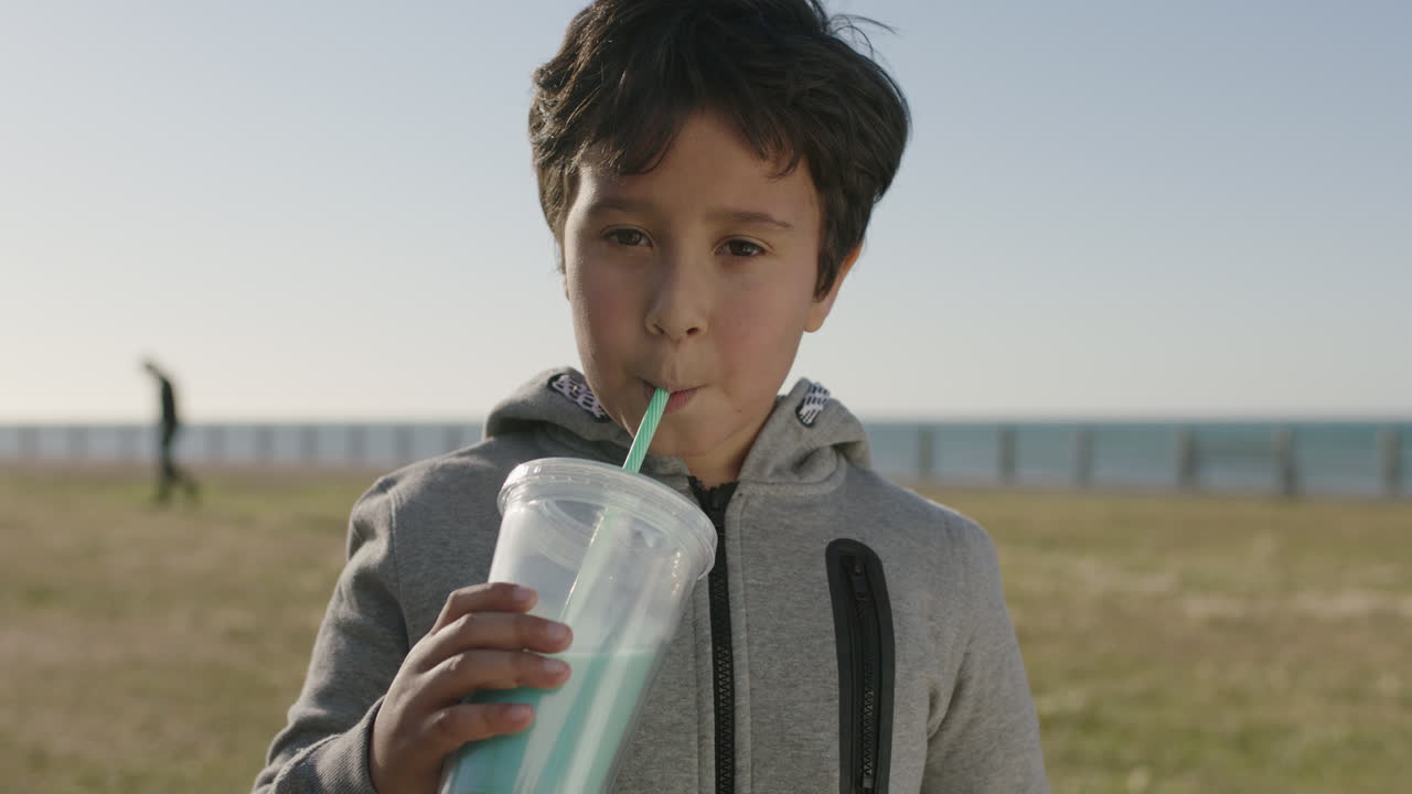 해변 공원에서  ⁇ 은 날을 즐기는 카메라를 바라보며 밀크셰이크 음료를 마시는 작은 히스패닉 소년의 초상화