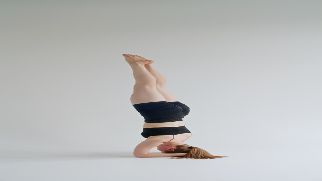 Young Woman Performing Headstand during Advanced Yoga Practice in White Studio