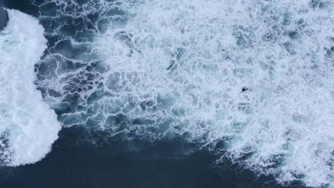 top down aerial view of bodyboarder ducking under crashing waves, rough seas