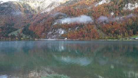 Left-to-right-pan-shot-of-a-lake-with-needle-forest-and-alpine-topography-mistic-clouds