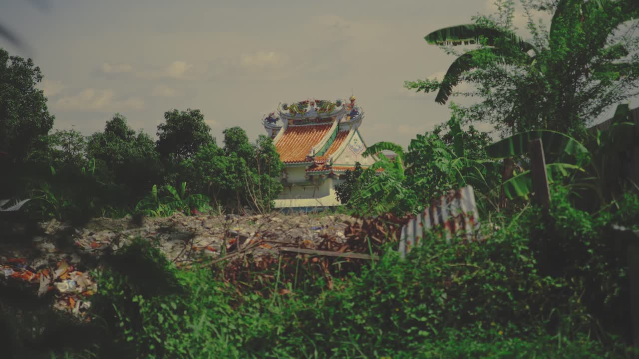 A Traditional Temple With an Ornate Rooftop Stands Amid Dense Greenery and Scattered Debris in Bangkok, Thailand - Wide Shot