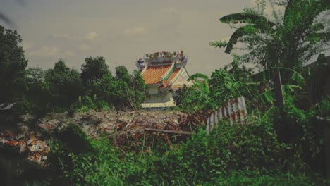 a traditional temple with an ornate rooftop stands amid dense greenery and scattered debris in bangkok, thailand - wide shot