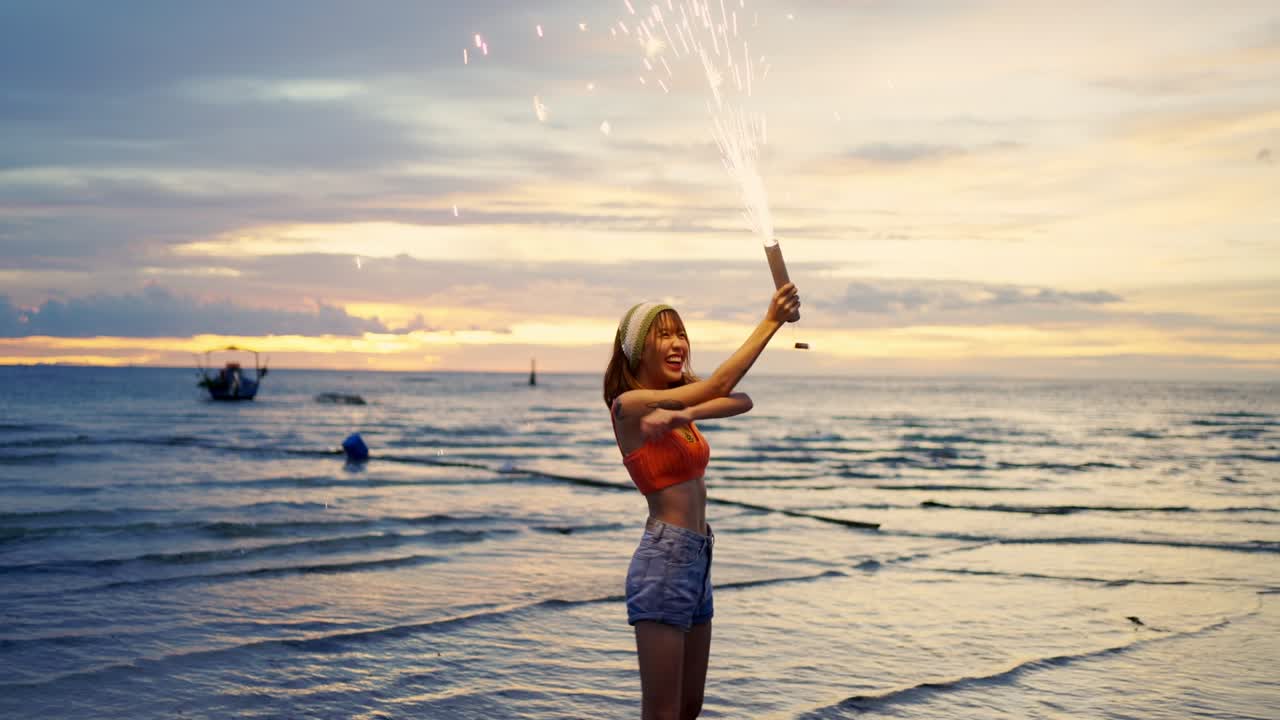 4K Asian woman playing sparklers on tropical island beach in summer night.