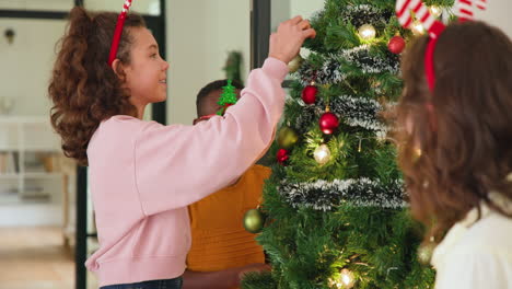 children decorating christmas tree at home, wearing festive headbands and glasses