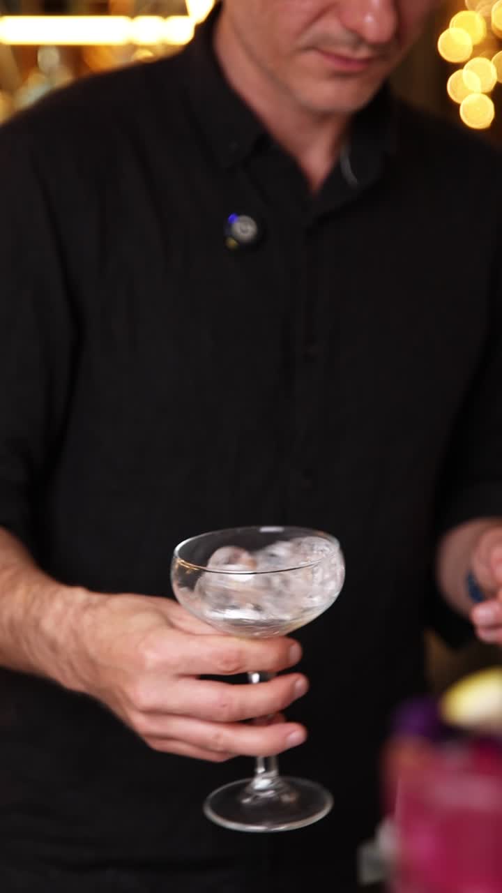 Barman che raffredda un bicchiere da cocktail con ghiaccio prima di preparare un drink
