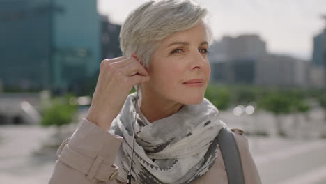 close up portrait of mature caucasian business woman wearing earphones listening to music looking relaxed in sunny urban city