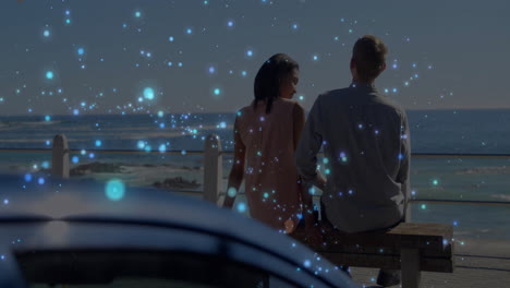 Sitting on bench by ocean, couple watching glowing blue animation particles