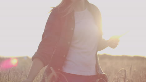 Close-up-of-a-woman-farmer-in-a-hat-and-a-plaid-shirt-touches-the-sprouts-and-seeds-of-rye-examines-and-enters-data-into-the-tablet-computer-is-in-the-field-at-sunset