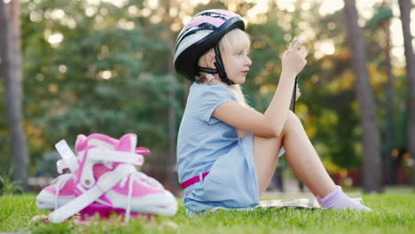 Ein-Mädchen-In-Einem-Schutzhelm-Spielt-Auf-Einem-Tablet-Neben-Ihr-Sind-Rollschuhe-HD-Video