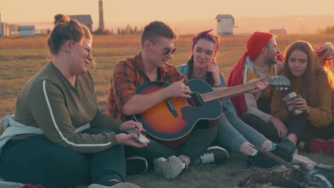 Un-Tipo-Toca-La-Guitarra-Descansando-Con-Amigos-En-El-Campamento-Al-Atardecer