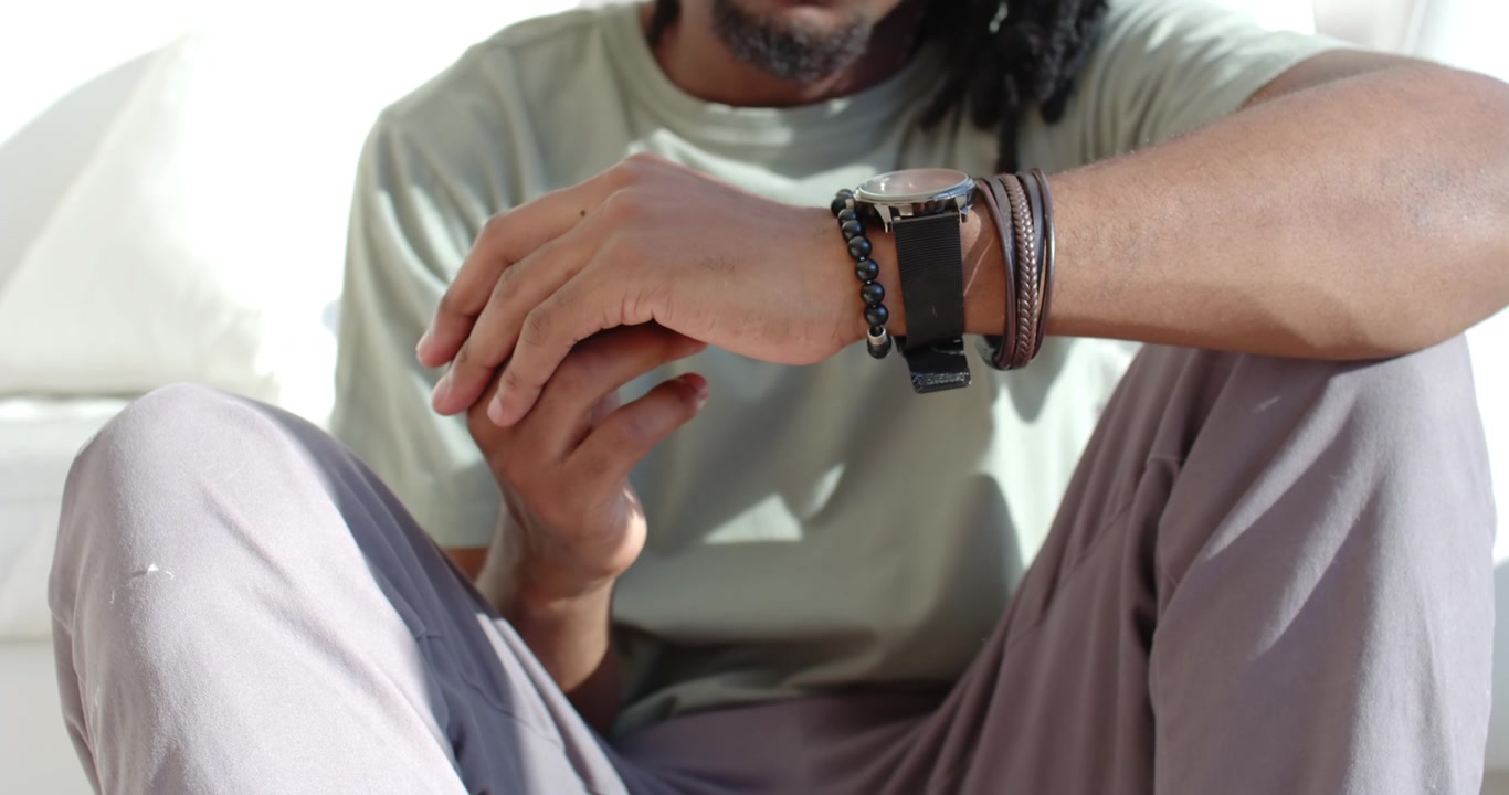 African American man after clasping hands, rubbing and rotating wrists on sofa wearing wristwatch