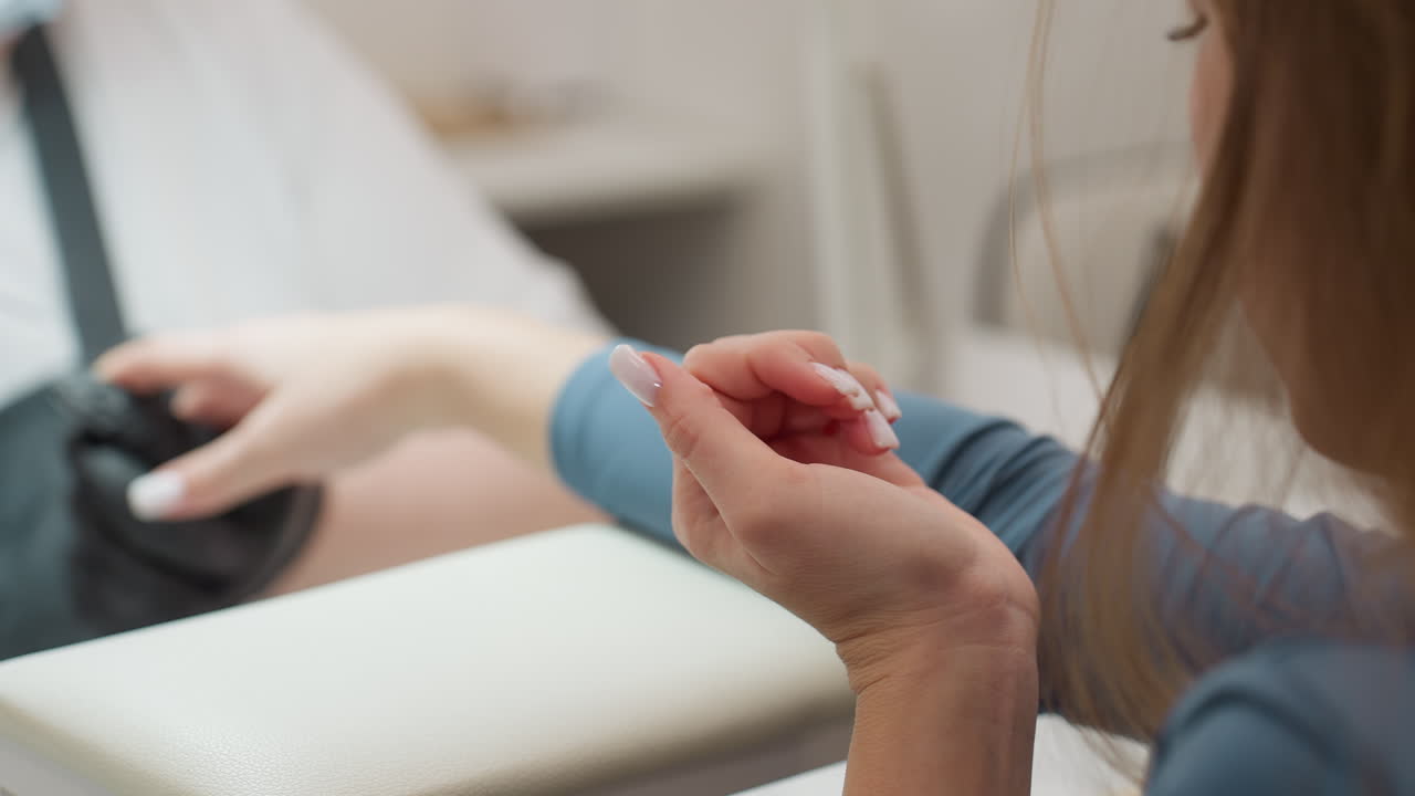 Client closely examines freshly applied acrylic nails while technician continues filing other hand. Moment captures satisfaction, precision, and beauty care in serene salon setting with soft lighting
