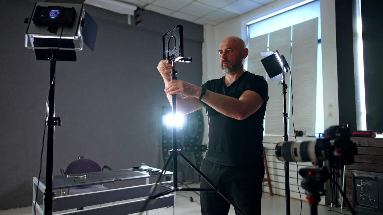 Photographer arranging equipment in photo studio. Bearded cameraman setting tripod with lens.
