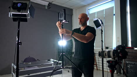 photographer arranging equipment in photo studio. bearded cameraman setting tripod with lens.