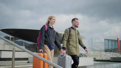 couple walking with suitcases near a fountain