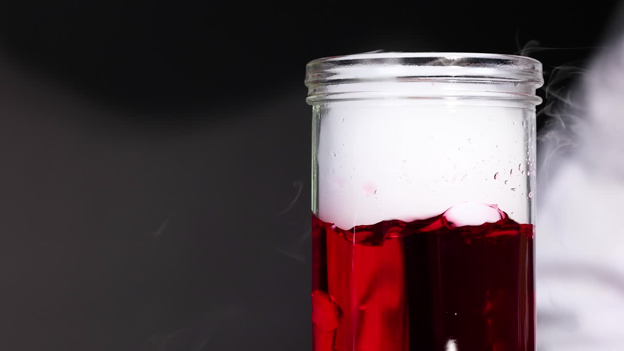 un vaso con líquido rojo reacciona con hielo seco, creando efectos de vapor dramáticos en un entorno controlado