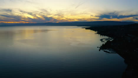 Hermosa-Vista-Azul-Y-Amarilla-De-La-Puesta-De-Sol-Sobre-Las-Orillas-Del-Lago-Leman-Lutry-En-Suiza---Toma-Aérea