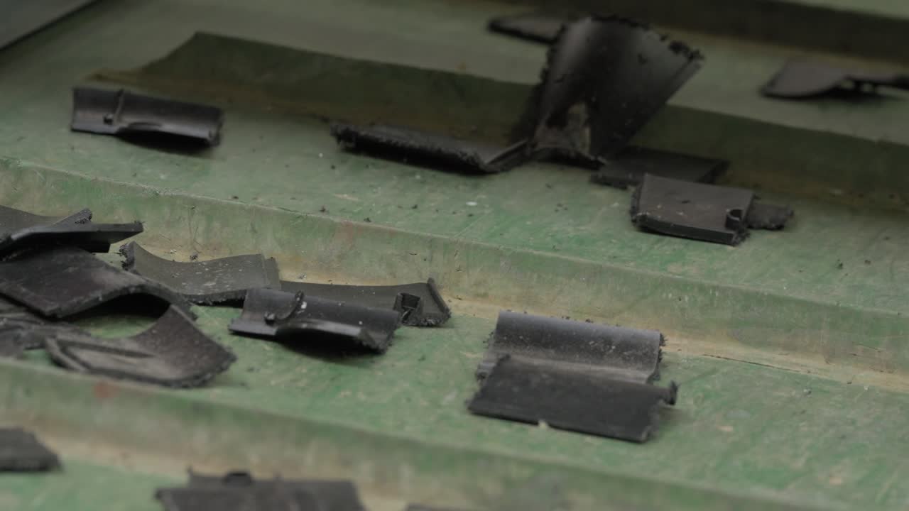 Large shredded black plastic chunks and fragments spread across green conveyor belt in recycling facility