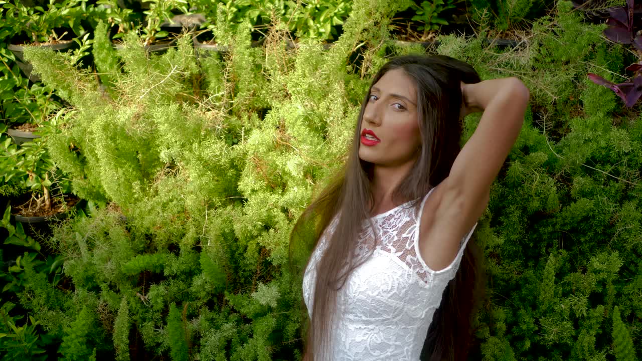 Experienced Female Photomodel in a White Dress With Long Hair Posing to a Camera by Green Mediterranean Plants, Full Frame
