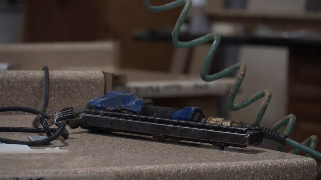 carpintero recoge una pistola de grapa de aire de la encimera en un taller de gabinetes