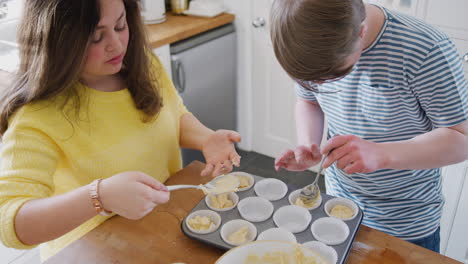 Junges-Paar-Mit-Down-Syndrom,-Das-Zu-Hause-In-Der-Küche-Mischung-In-Papierkuchenförmchen-Gibt