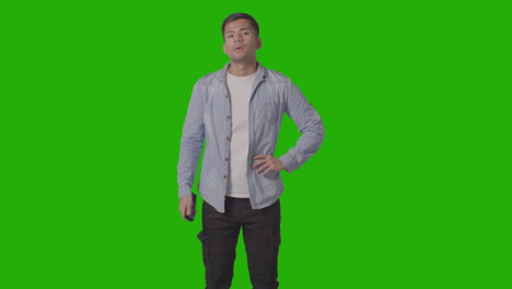 studio shot of casually dressed young man with remote control flicking through tv channels against green screen 2