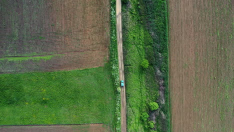 Drone-Siguiendo-A-Un-Automóvil-Conduciendo-Por-Un-Camino-De-Tierra-Húmedo-Con-Muchos-Vendedores-Ambulantes-De-Agua