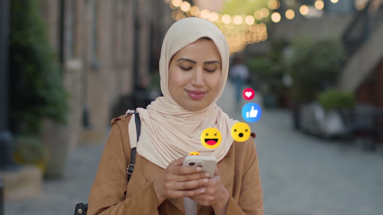 Muslim Woman Walking Along City Street Looking At Mobile Phone With Motion Graphics Emojis Showing Multiple Networking Messaging And Social Media Notifications