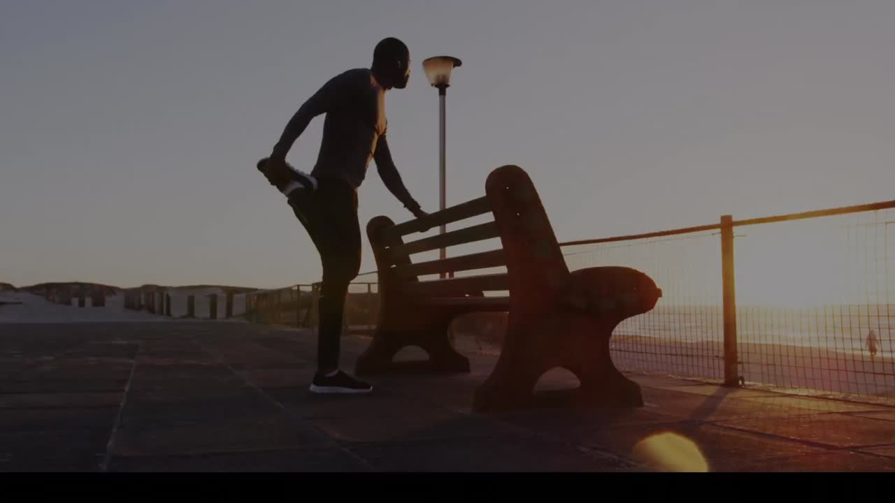 Spots of light against african american fit man stretching his leg near a bench at the promenade