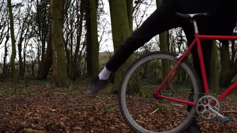 man stands up and cycles away in a forest on a red bike