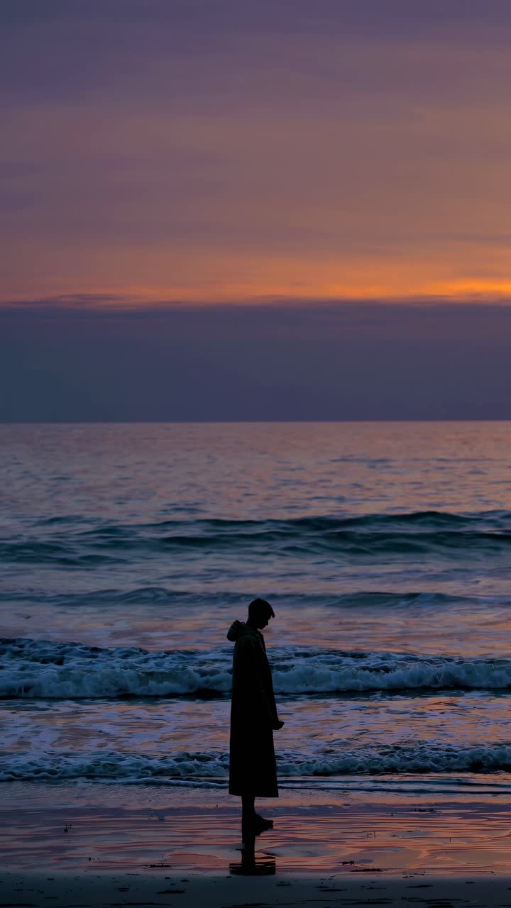 Silhouette of a person on a beach at sunset, captured from a side angle