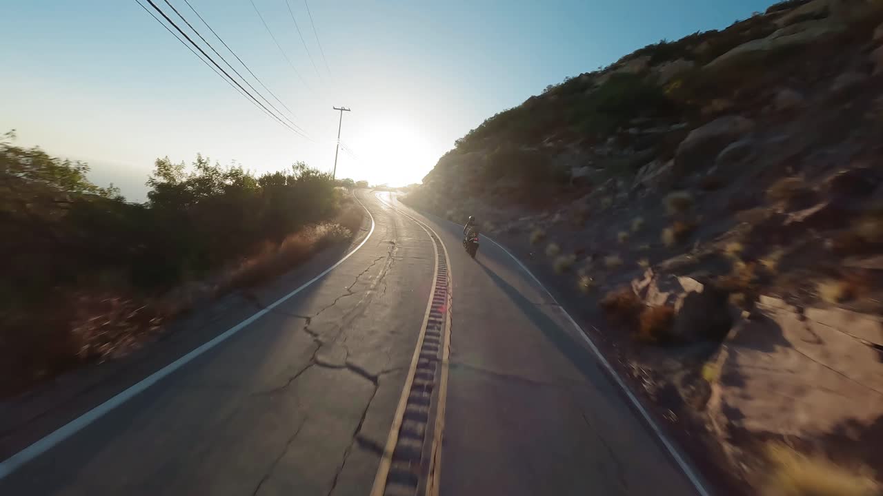 fpv drone flyover topanga sinuoso camino sigue motociclista truco mientras hace un caballito, luz solar brillante, california