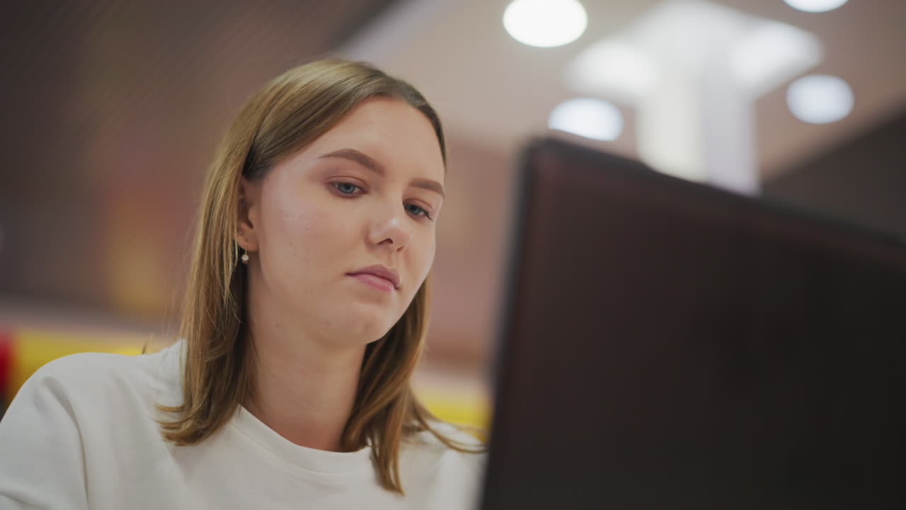 primer plano de una mujer joven escribiendo atentamente en una computadora portátil en un entorno interior moderno con un fondo colorido borroso, que irradia enfoque profesional y dedicación
