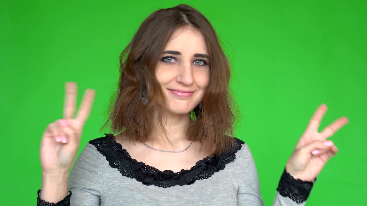 Young woman showing victory or peace sign while looking at the camera over green background.